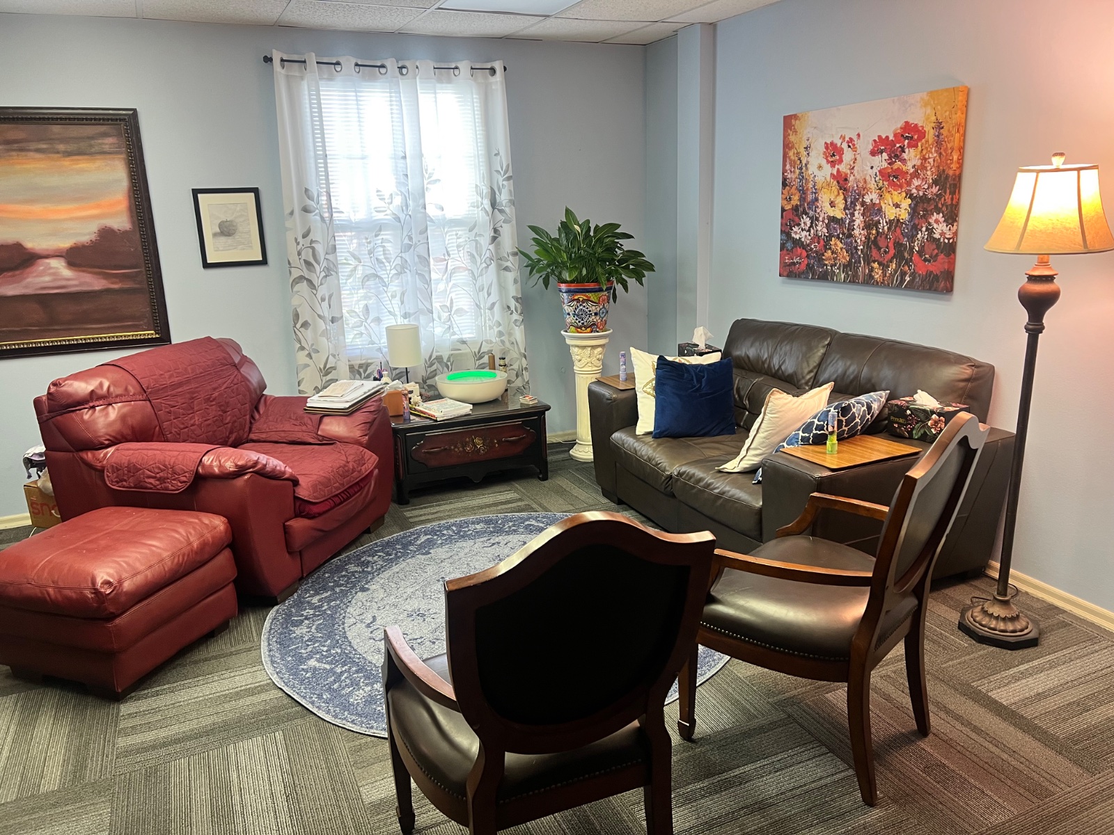 Bright, naturally lit view of Cynthia Benedict's Longwood counseling office with leather sofa, red armchair and floor lamp