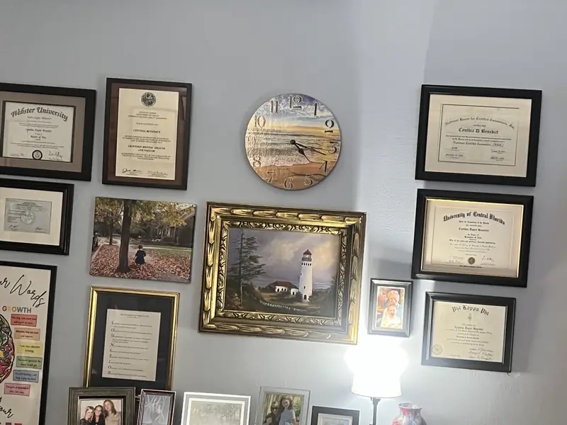 Wall of framed degrees and licenses in Cynthia Benedict's Longwood counseling office
